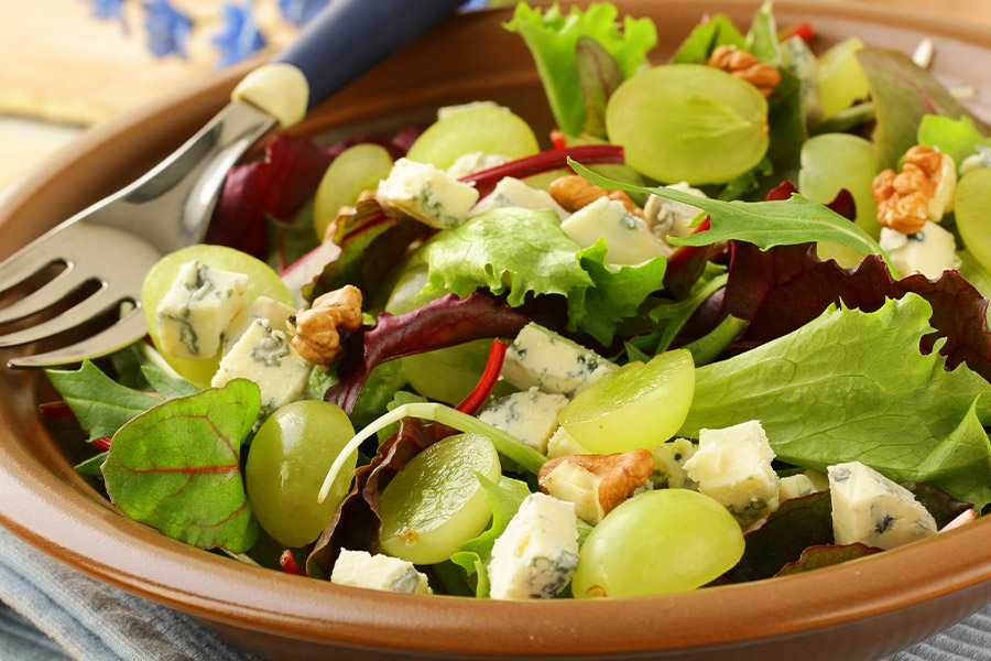 Braune Schüssel gefüllt mit appetitlich buntem Salat bestehend aus Blattsalaten, Weintrauben, Walnüssen und Käse.