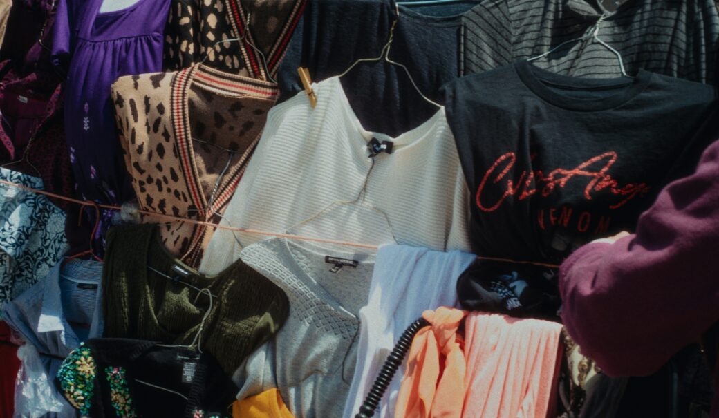 Viele unterschiedlich bunte Kleidungsstücke hängen auf Wäscheleinen gespannt auf einem Flohmarkt